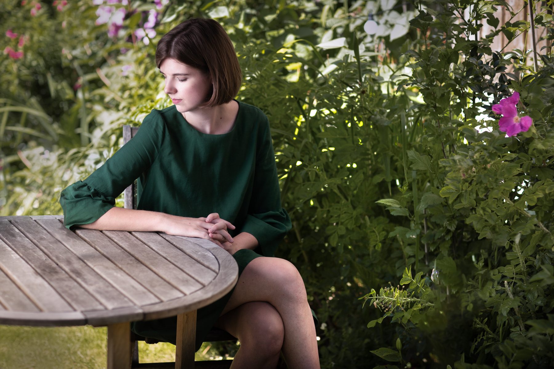 Elizabeth MacNeal, author, in a green smock dress in her garden, portrait by Mat Smith Photography, East London