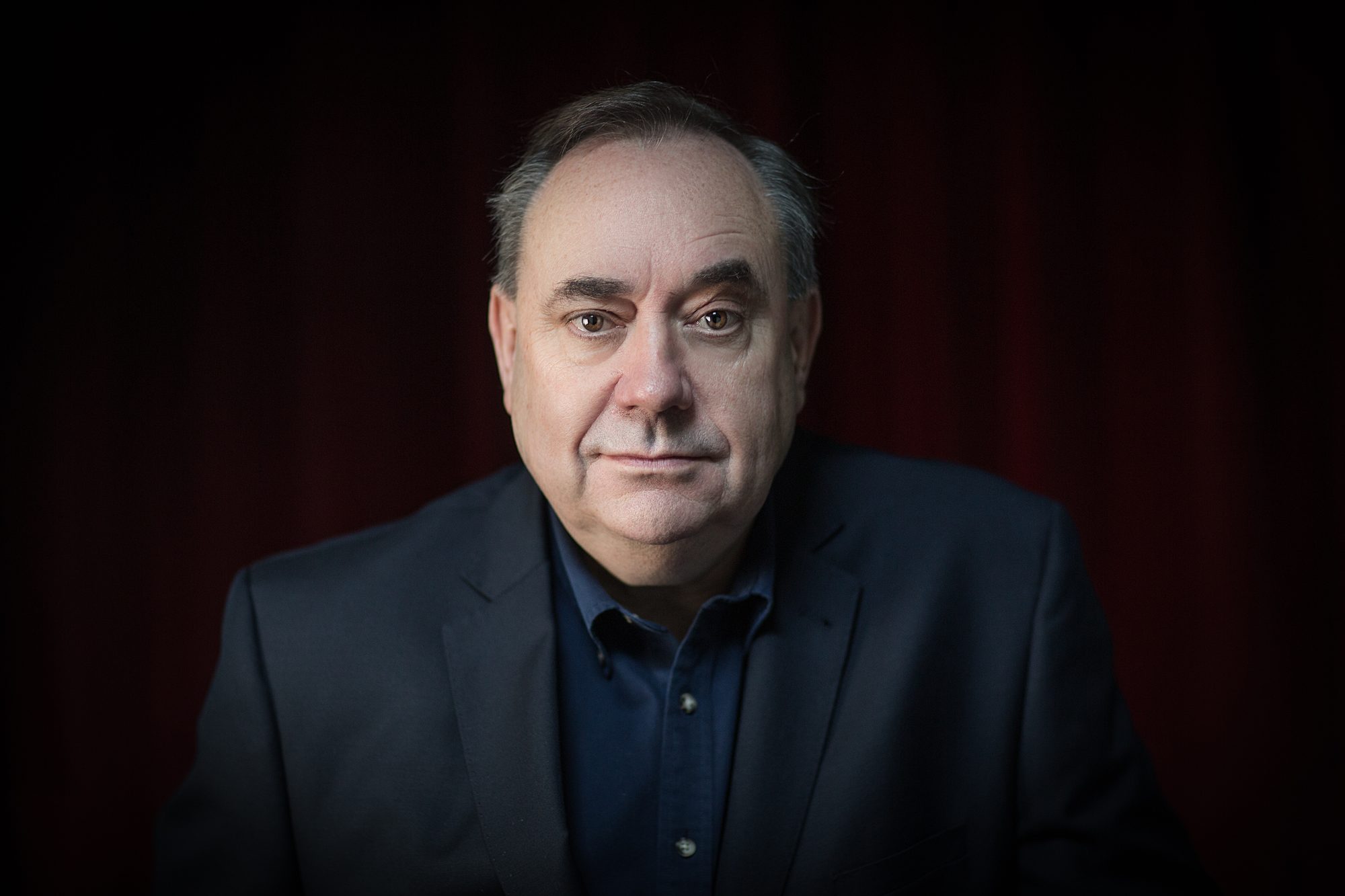 Close portrait of Alex Salmond against a dark red curtain