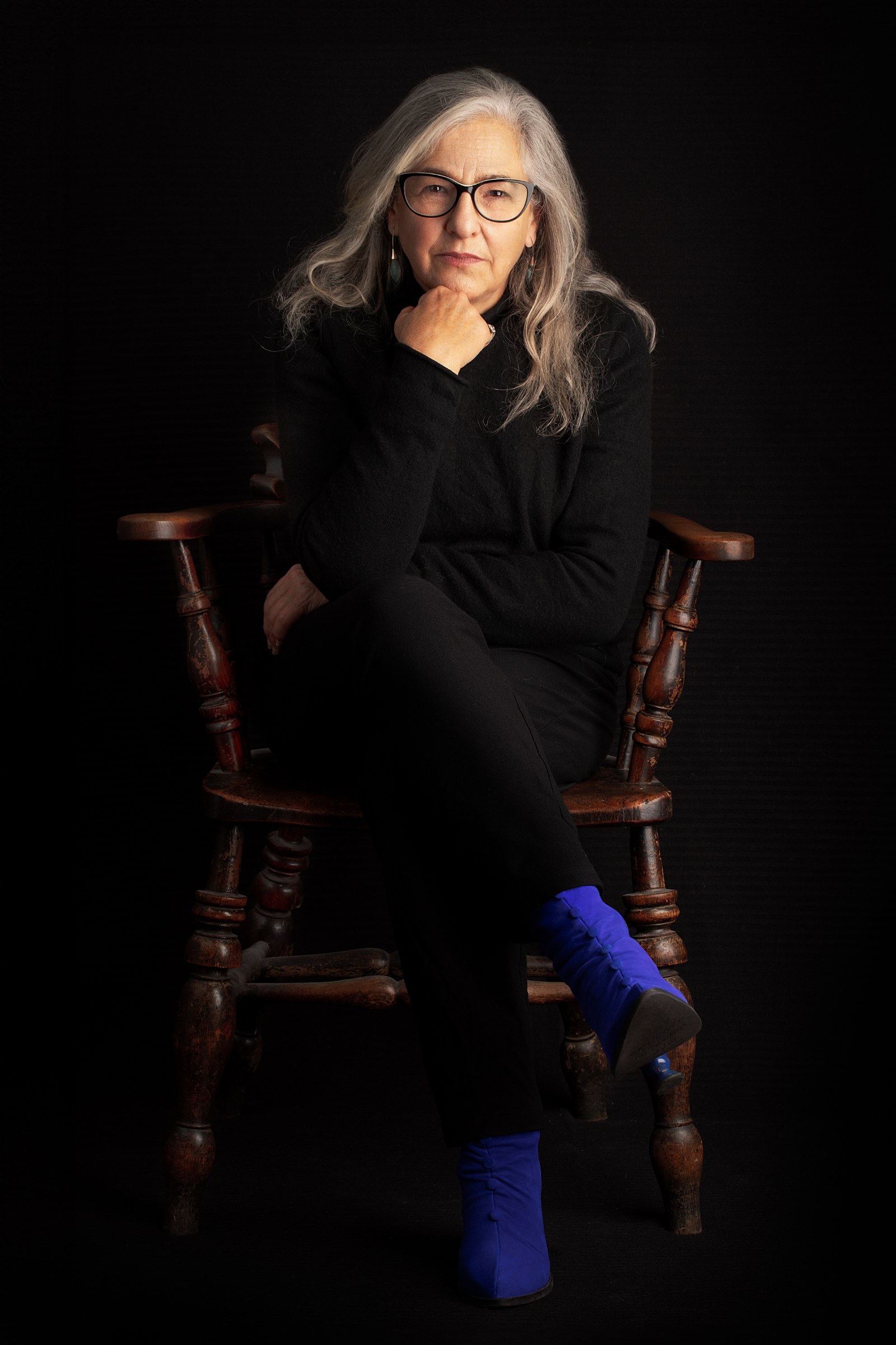 Karen Liebreich MBE, author and historian, seated in a wooden chair in blue boots, colour portrait by Mat Smith Photography, Chiswick
