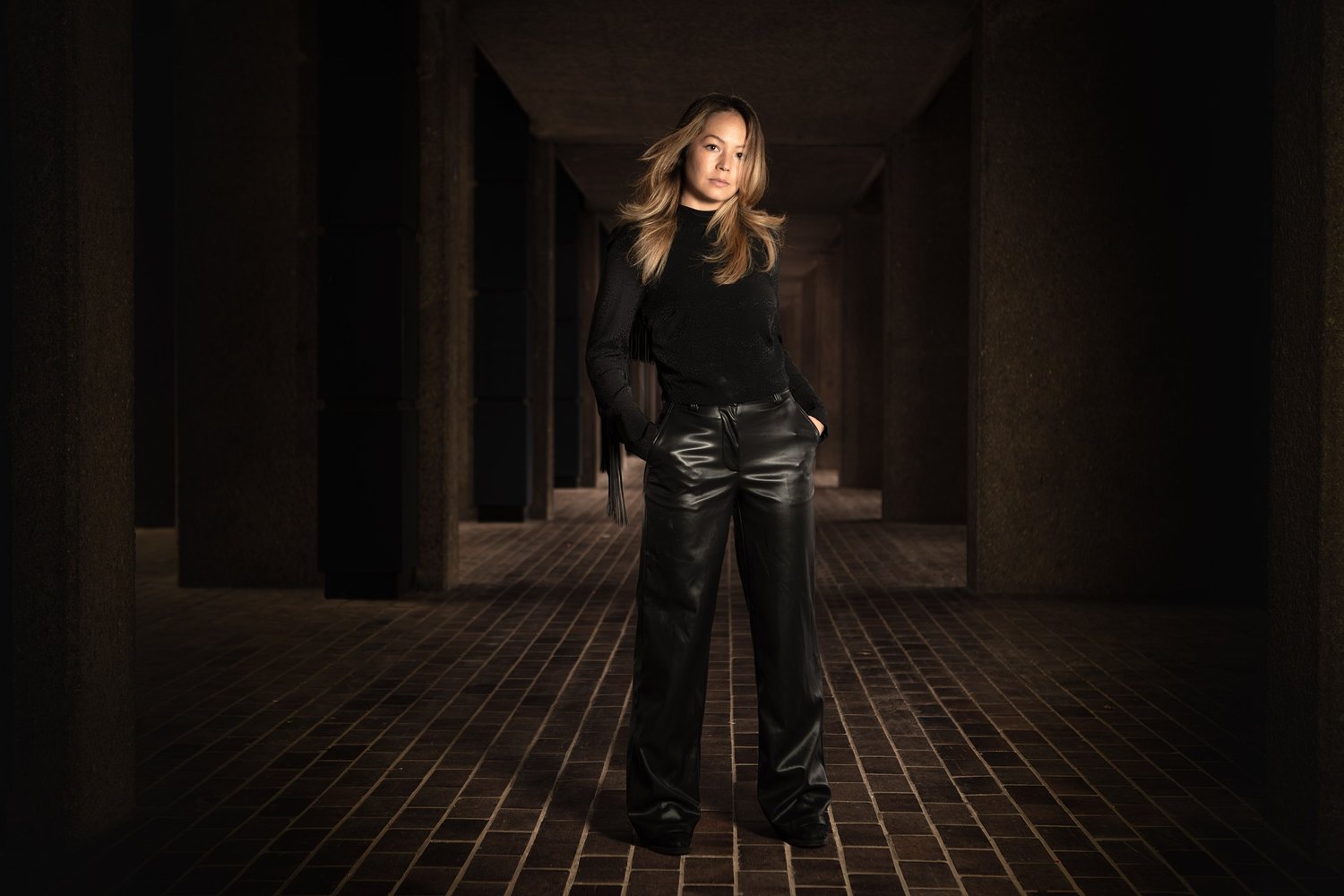 Emily Lim, composer, standing in a long concrete walkway, portrait by Mat Smith Photography, the Barbican, London