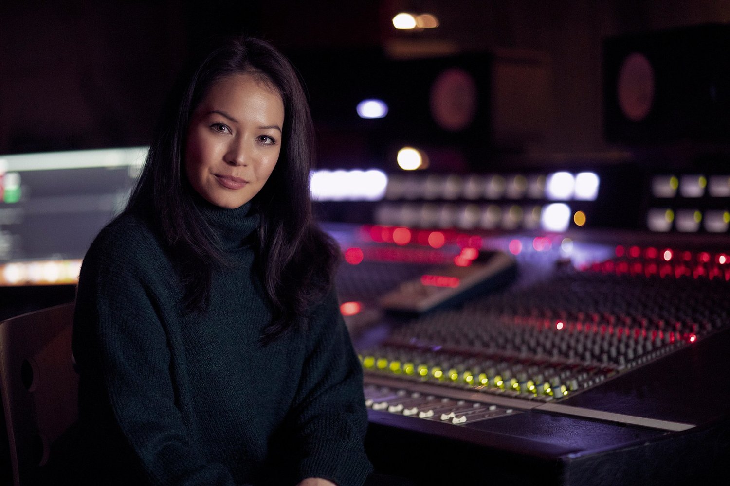 Emily Lim, composer, seated beside a lit mixing desk in a recording studio, portrait by Mat Smith Photography, north west London