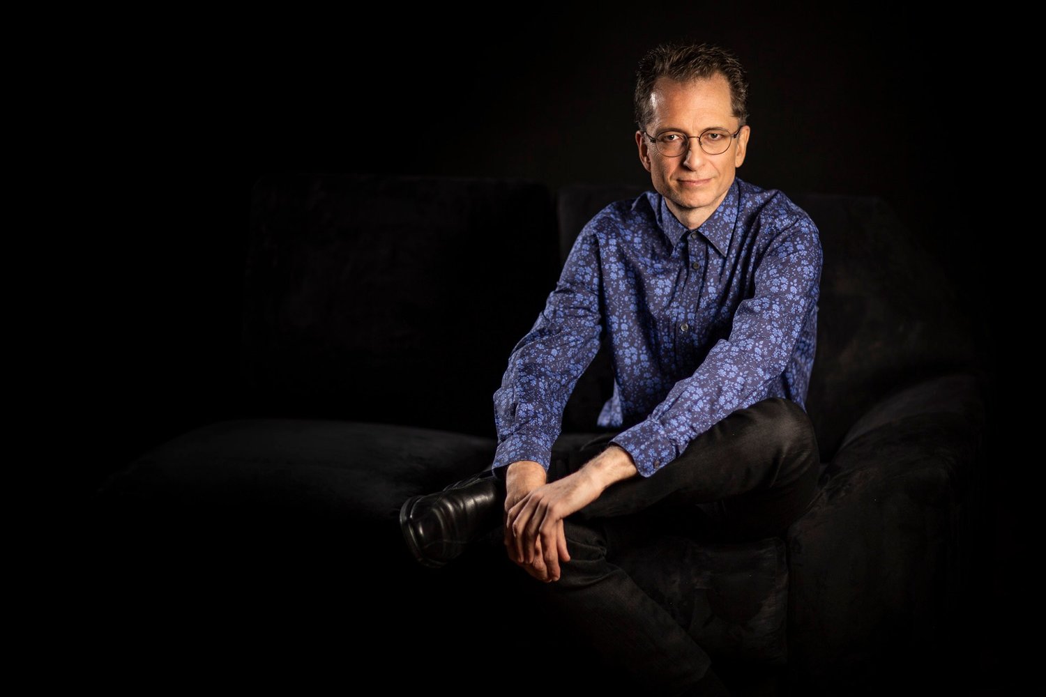 Gavin Greenaway, composer and conductor, seated on a dark sofa in a recording studio, portrait by Mat Smith Photography, Hampstead, London