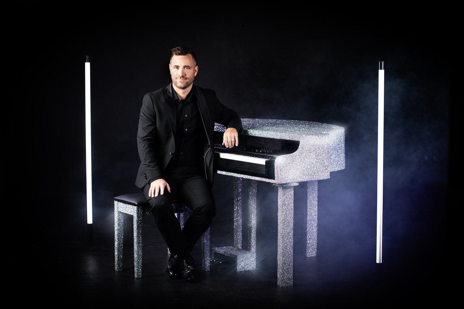 Michael Raggatt, pianist, seated beside a glittering silver piano between two light tubes, portrait by Mat Smith Photography
