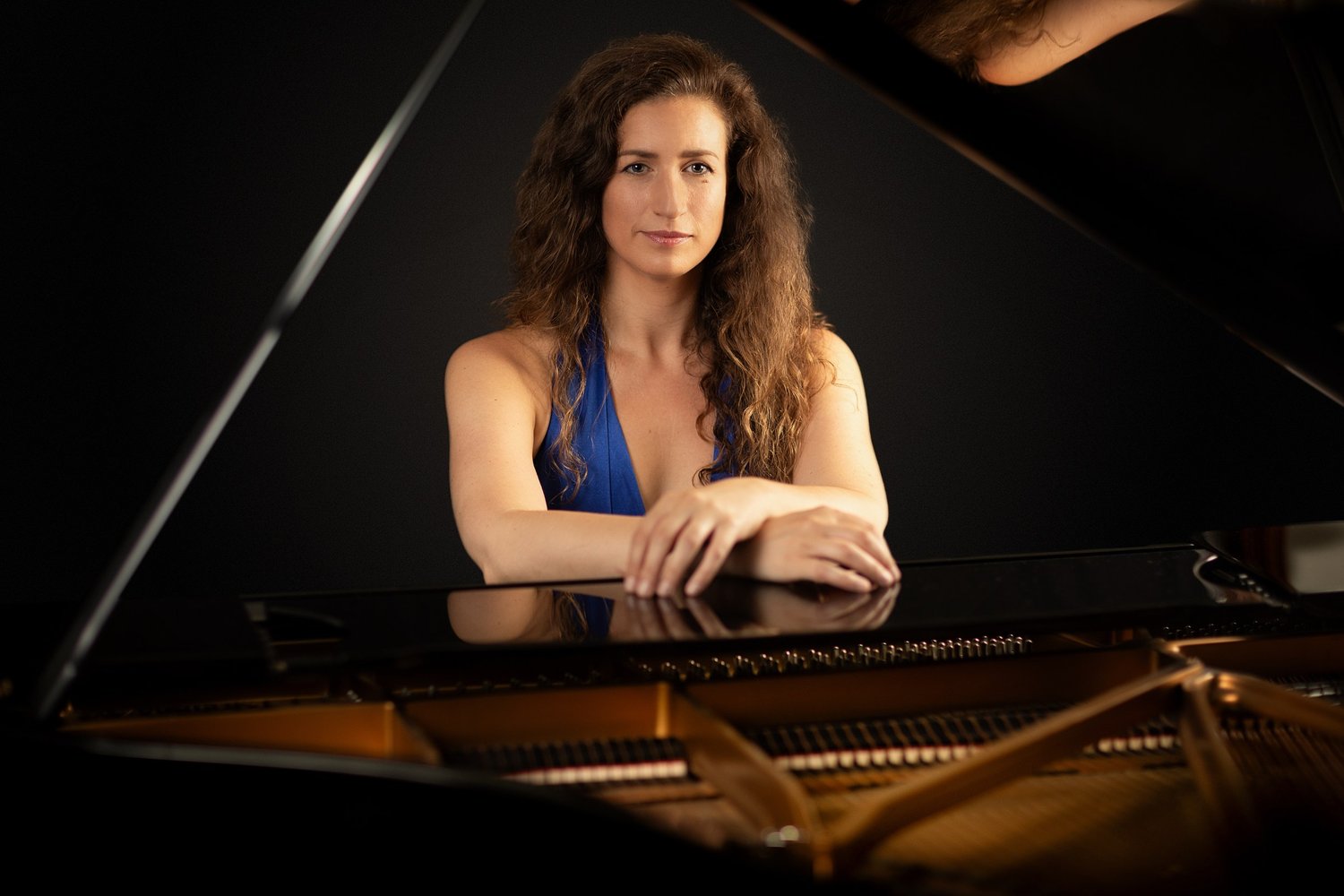 Nadine André, pianist and piano teacher, leaning on a grand piano in a blue dress, portrait by Mat Smith Photography