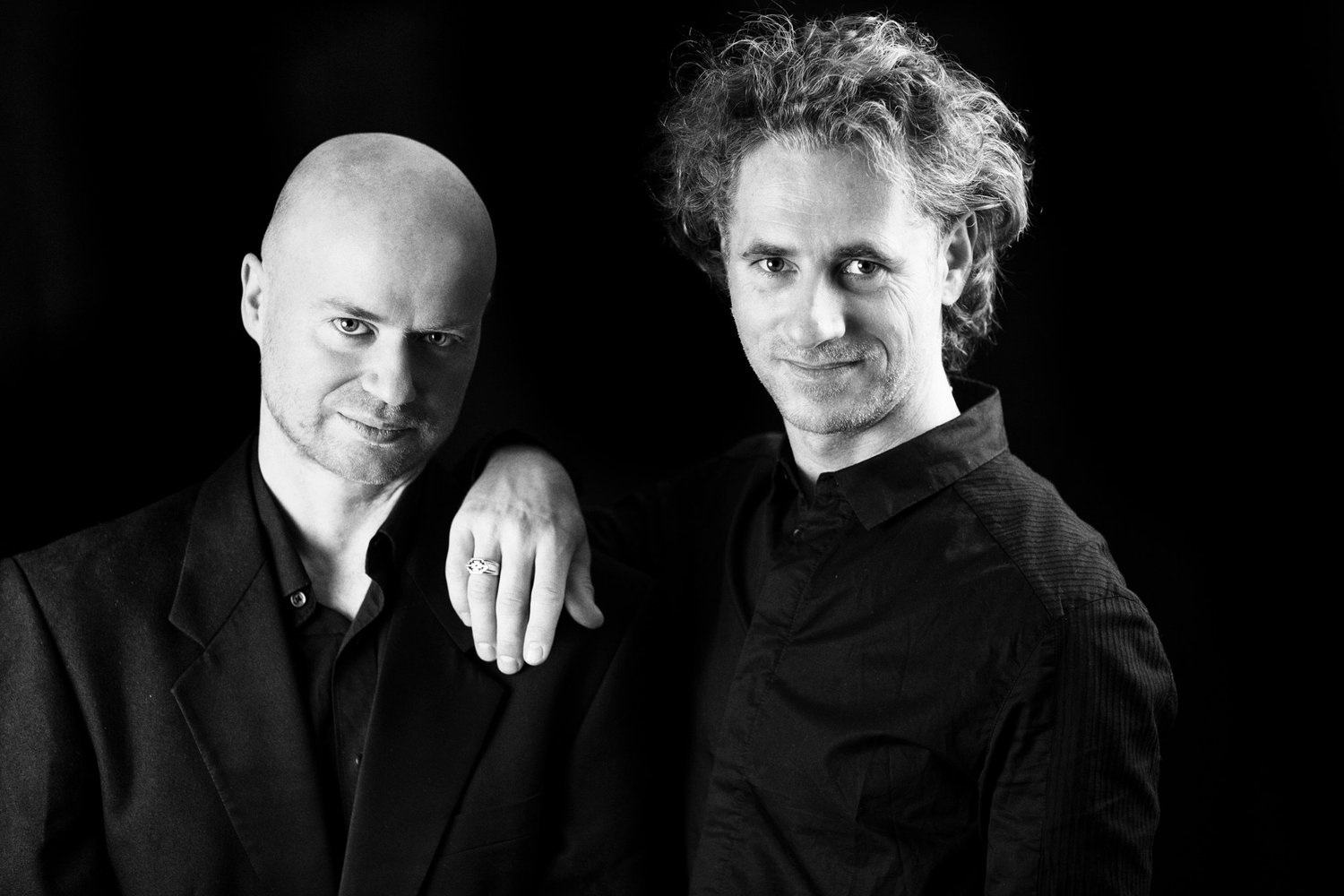 Patrick Savage and Holeg Spies, composers, in a black and white duo portrait on black, portrait by Mat Smith Photography