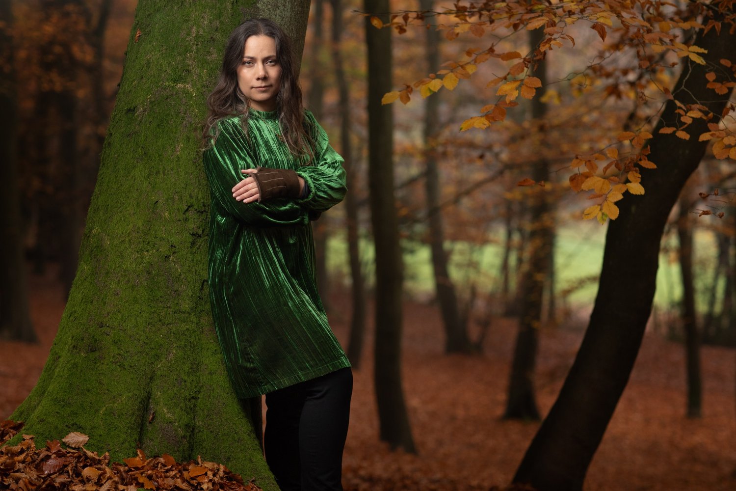 Rebecca Knight, cellist, in a green velvet dress leaning against a mossy beech trunk among autumn trees, portrait by Mat Smith Photography, Chiltern beech woods, Beaconsfield
