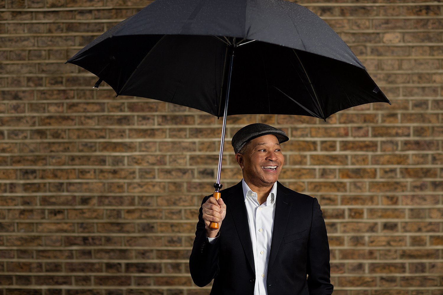 Smiling man against a brick wall, photographed in the rain in London