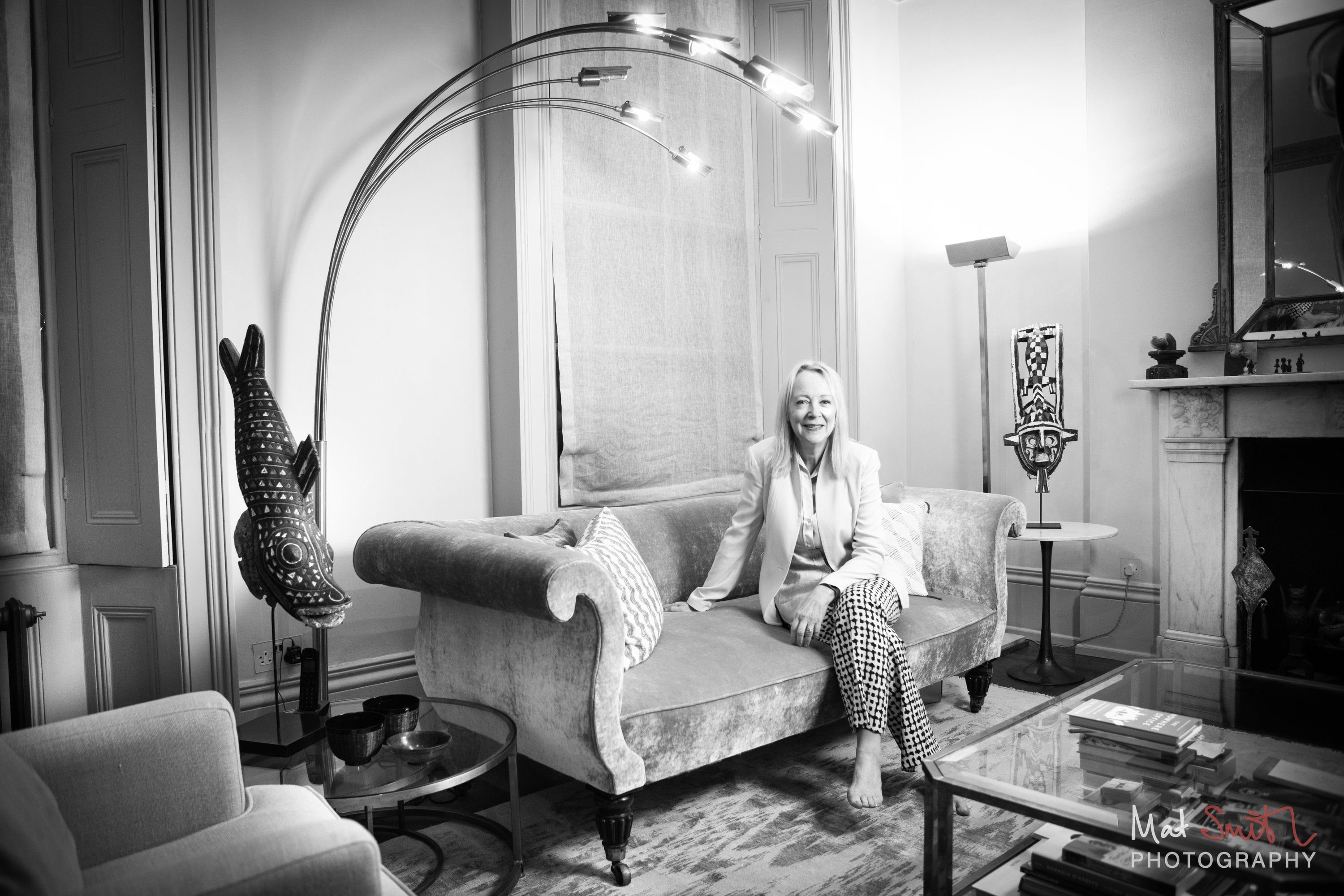 Black and white wide portrait of a woman on a velvet sofa in a drawing room with an arc lamp and tall windows, portrait by Mat Smith Photography, London
