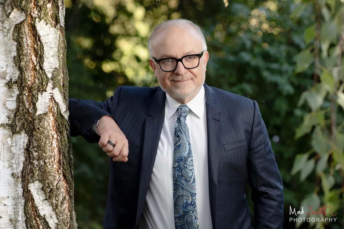 Professor leaning against a silver birch with green leaves behind, portrait by Mat Smith Photography, London